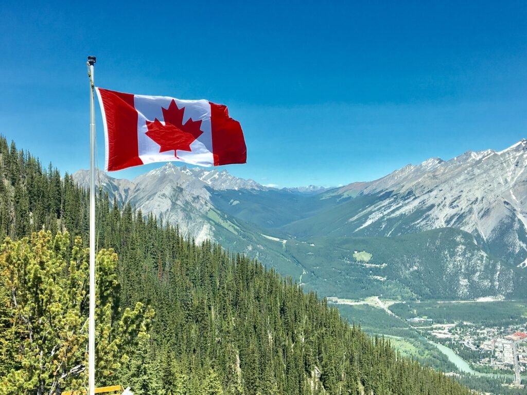 pexels-photo-756790-756790 - How To Apply Doc Canadian flag waving atop a scenic mountain view with blue skies and lush greenery.